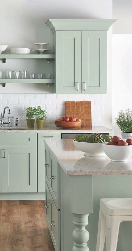 A soft green kitchen cabinets with a white marble countertop.