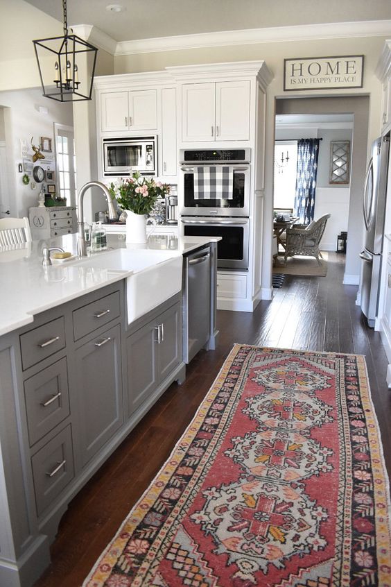 A grey kitchen island with a farmhouse sink and an oriental rug. 