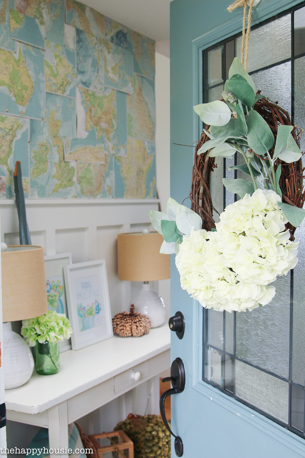 The front door is ajar showing a small white console table and a large map on the wall.