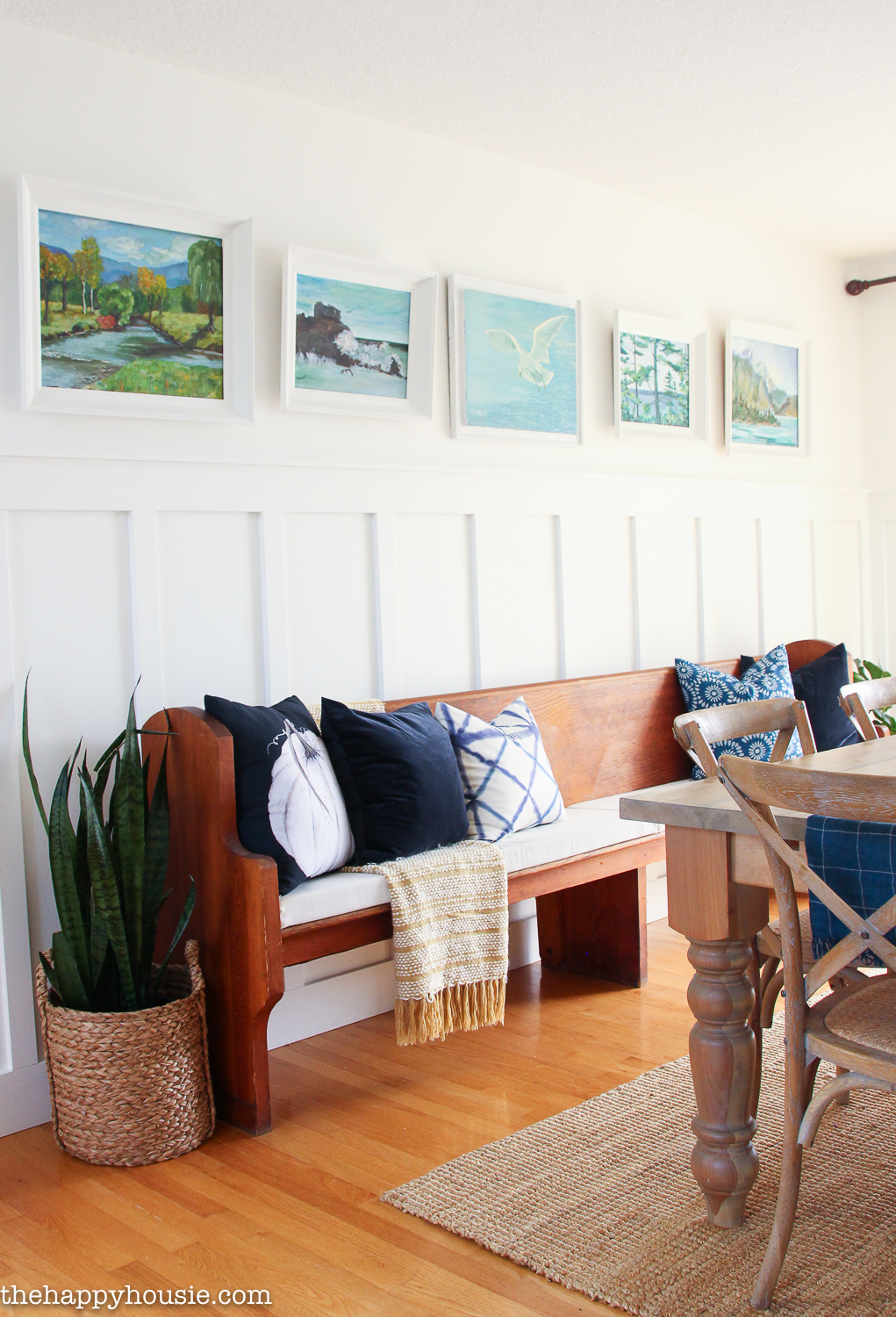 A wooden bench with pillows is on the board and batten wall in the dining room.