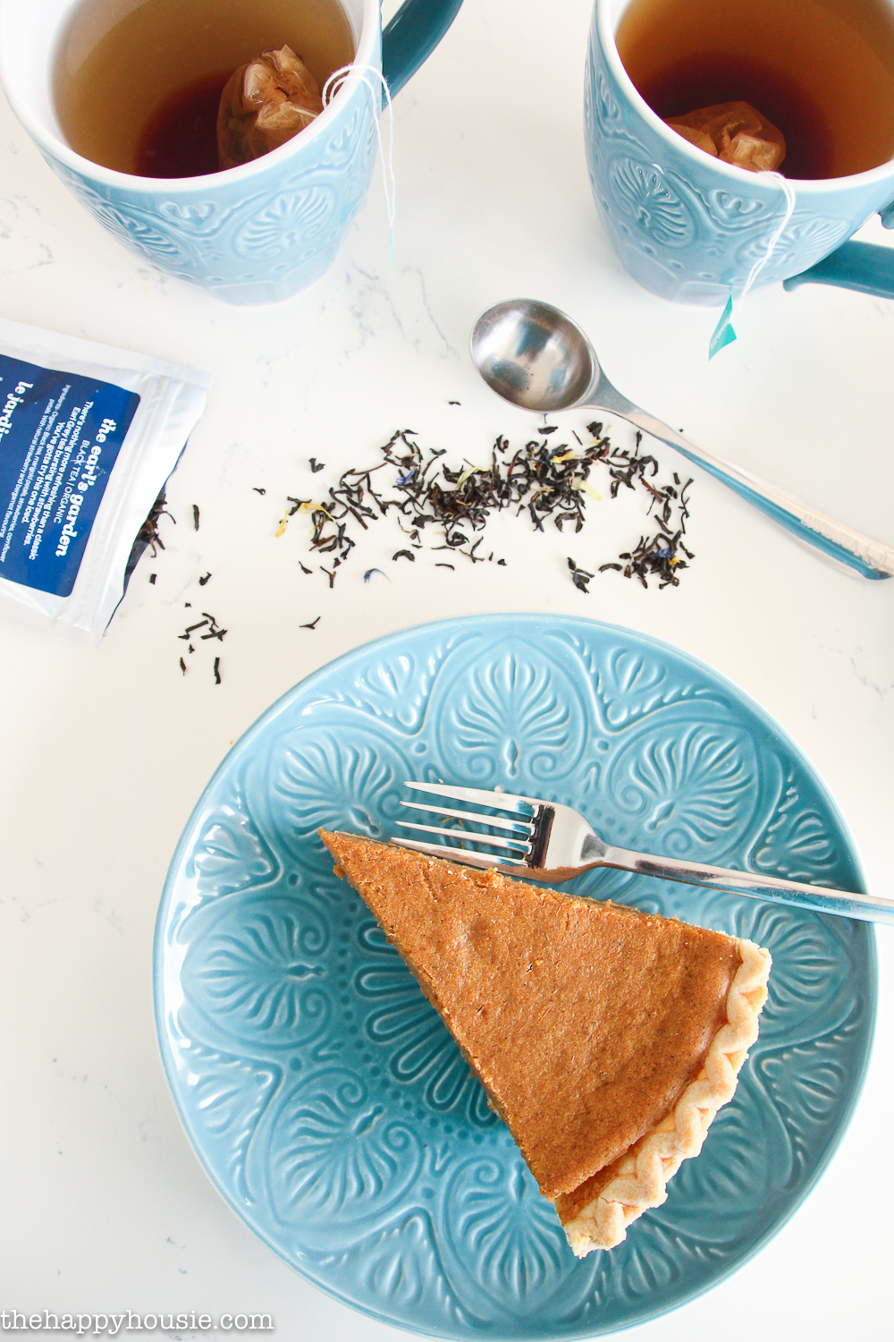 A slice of pumpkin pie on a blue plate with a cup of tea beside it.