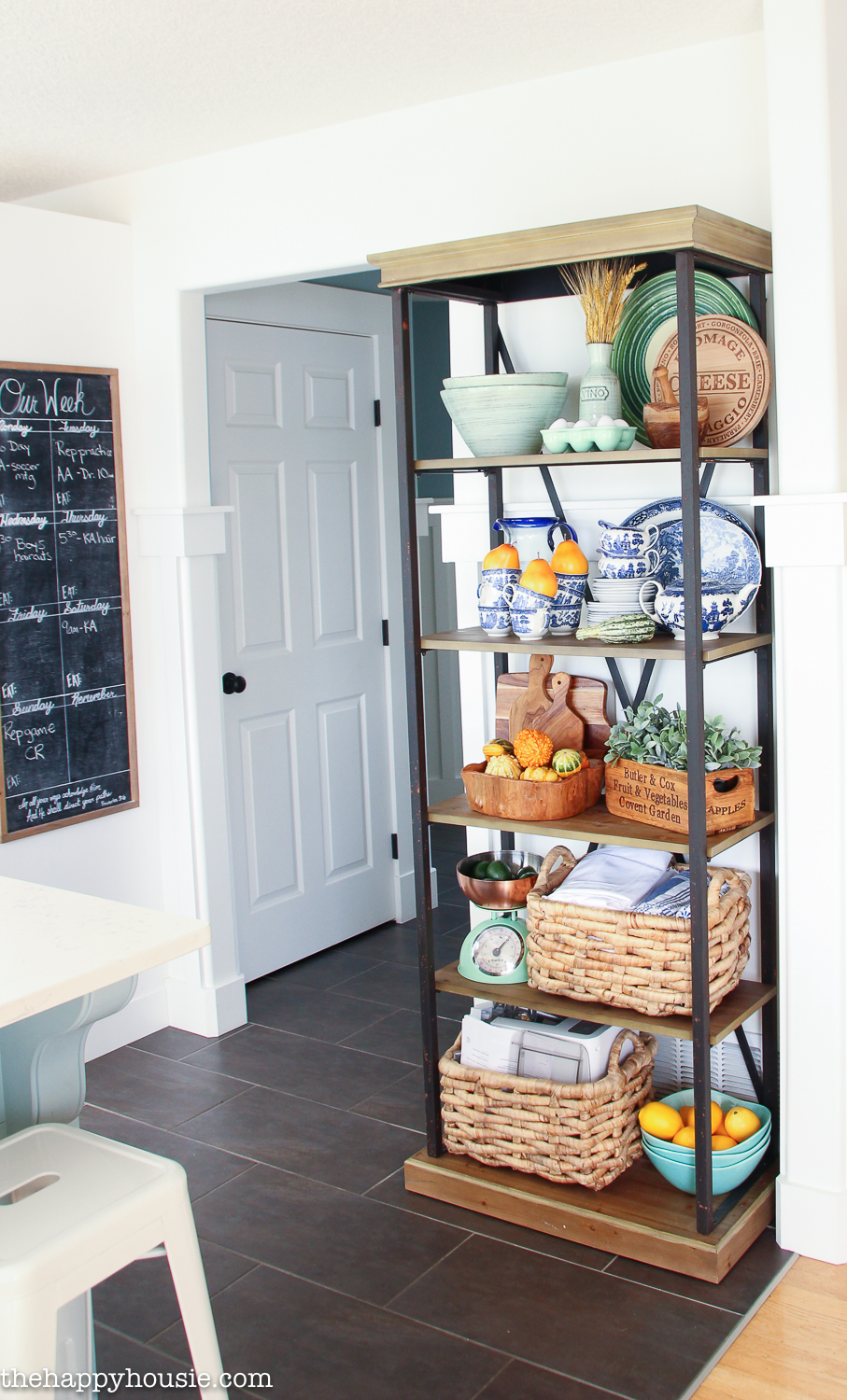 A wood and metal shelving unit in the kitchen contains baskets and plates.