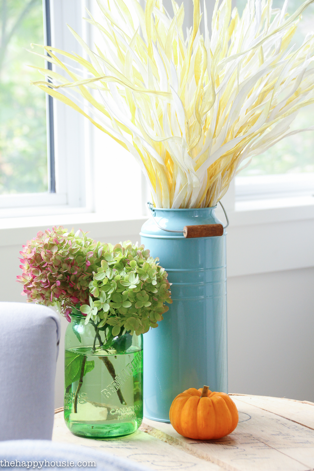 There are hydrangeas in a clear green vase beside the wheat stalks.