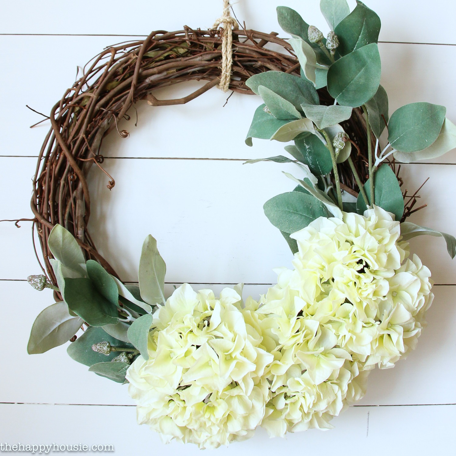 A grapevine wreath with white large flowers and eucalyptus leaves on it.