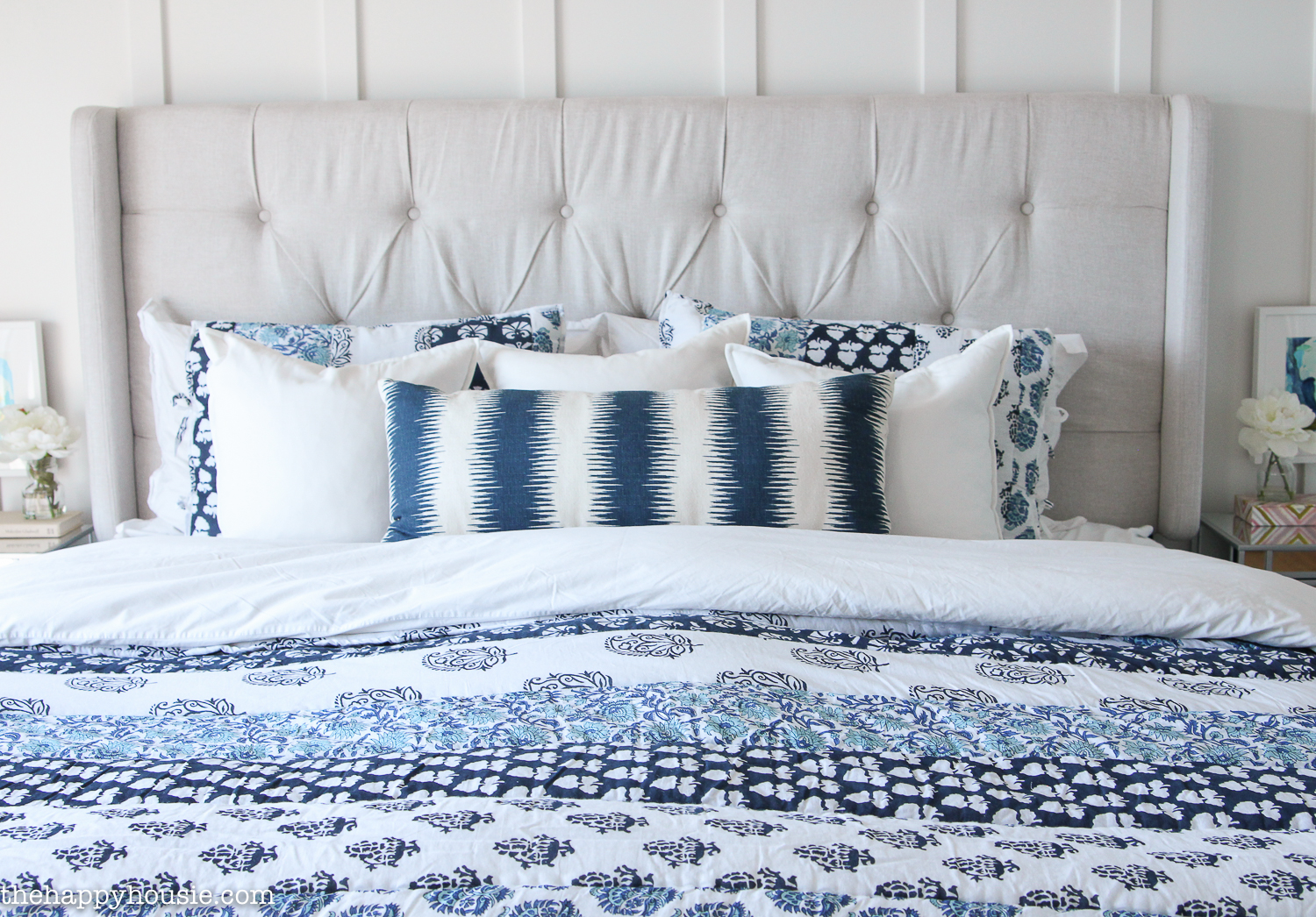 A cozy quilt on a king sized bed with a tufted white headboard.