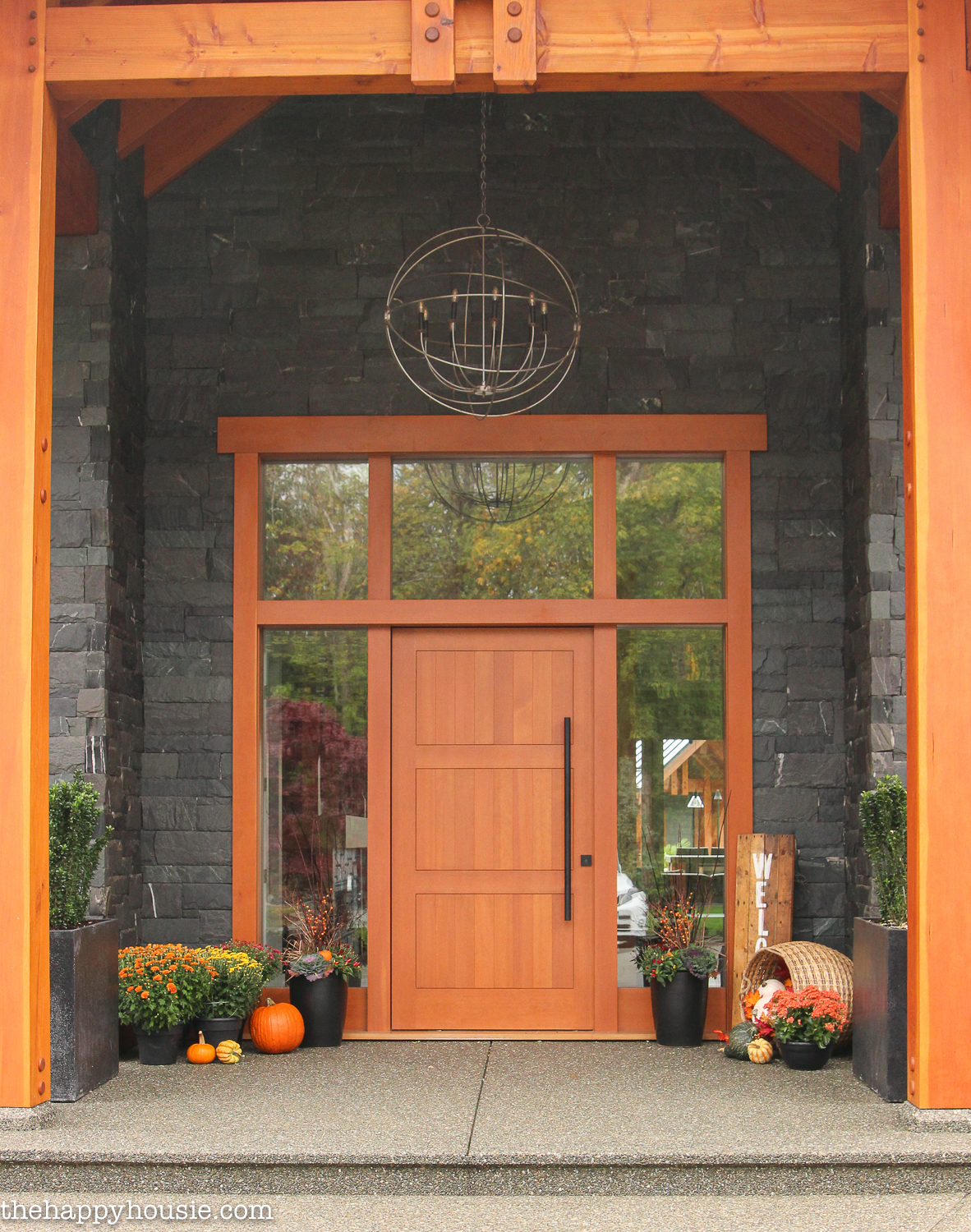A wooden frame and door surrounding brick with the porch decorated for fall.