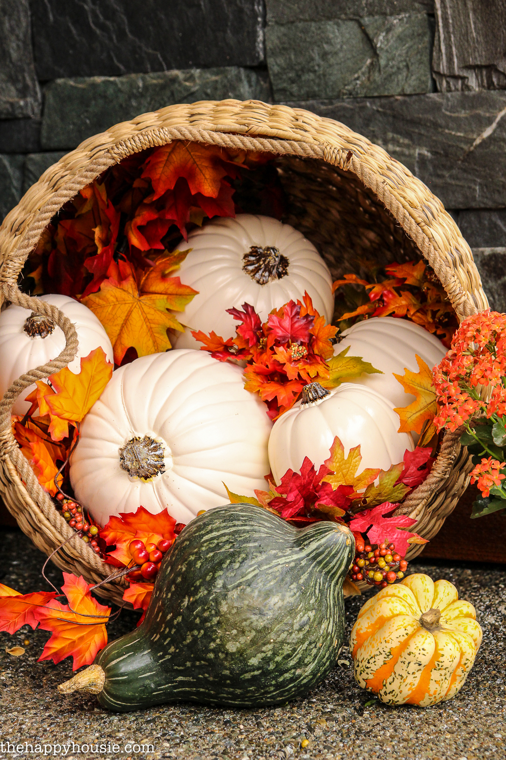 A basket tipped onto its side with faux leaves and white pumpkins and gourds.
