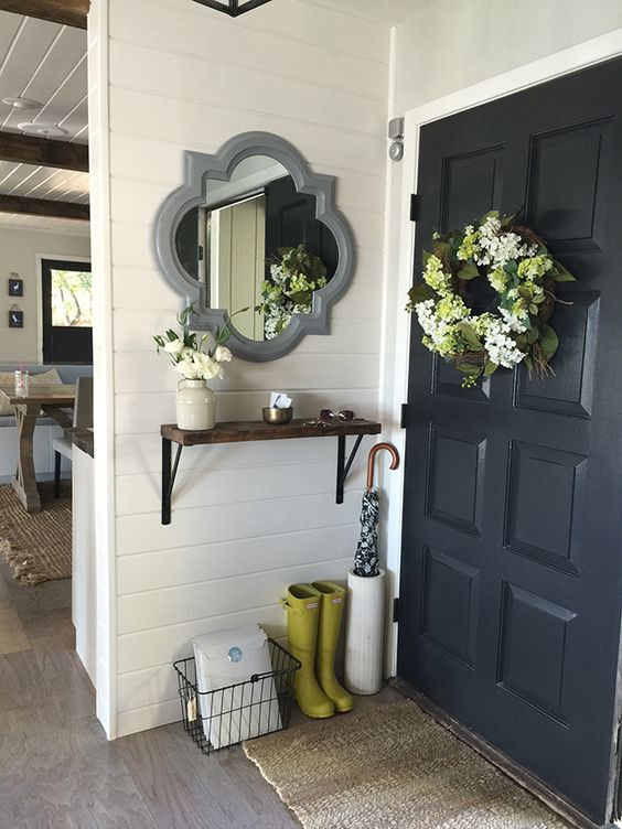 A decorative mirror is above a small wooden shelf with boots and an umbrella holder by the front door.