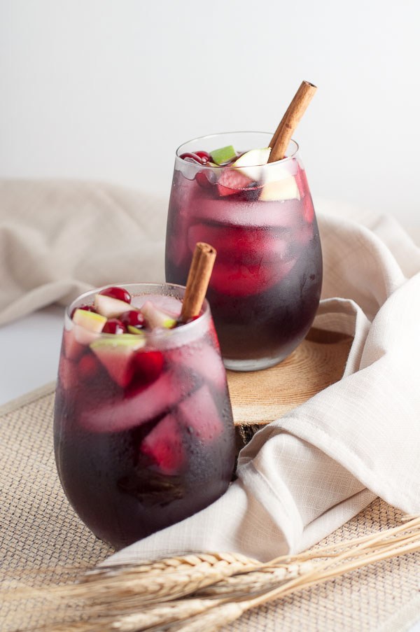 Cranberry apple cider in clear glasses with a stick of cinnamon.