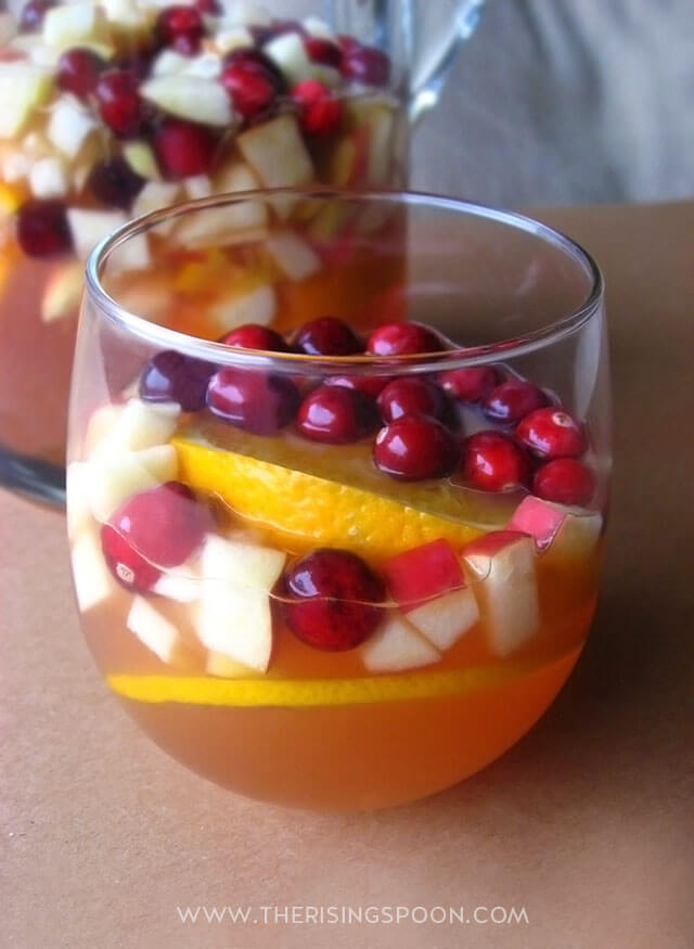 White wine sangria with cranberries and orange slices inside it.