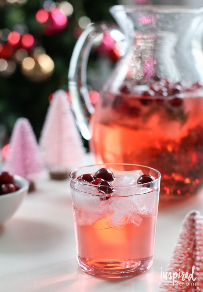 Jingle juice punch in a pitcher with a glass poured and cranberries on top.