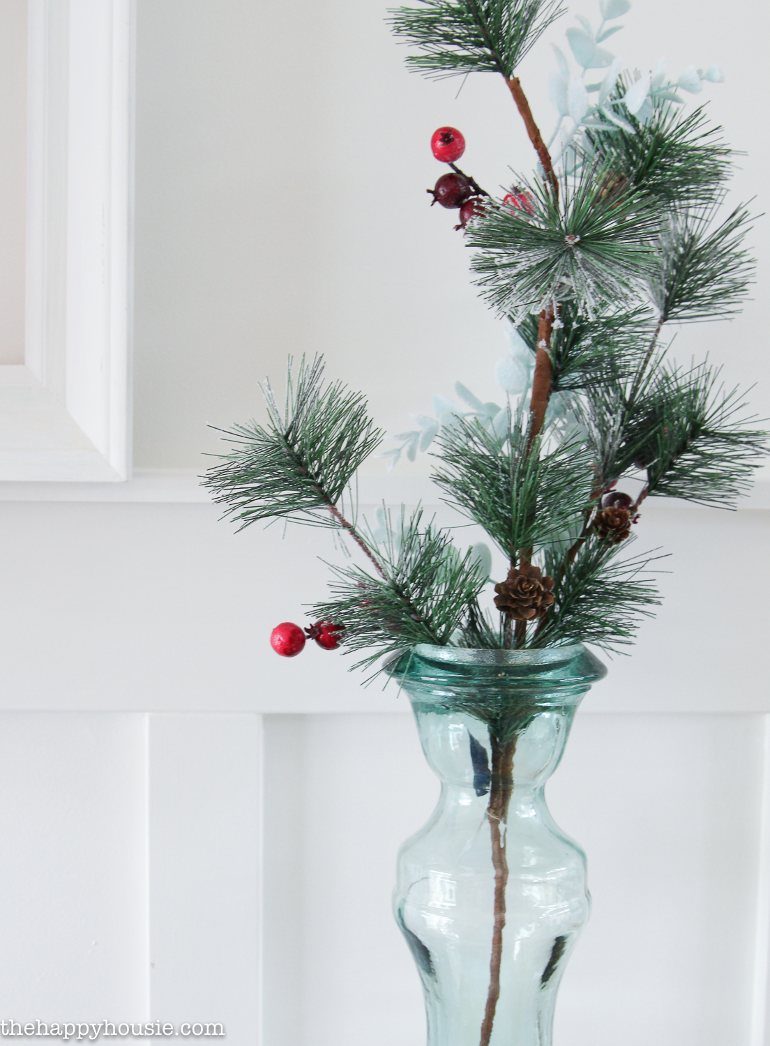 A single branch of evergreen with red berries is in clear glass vase.