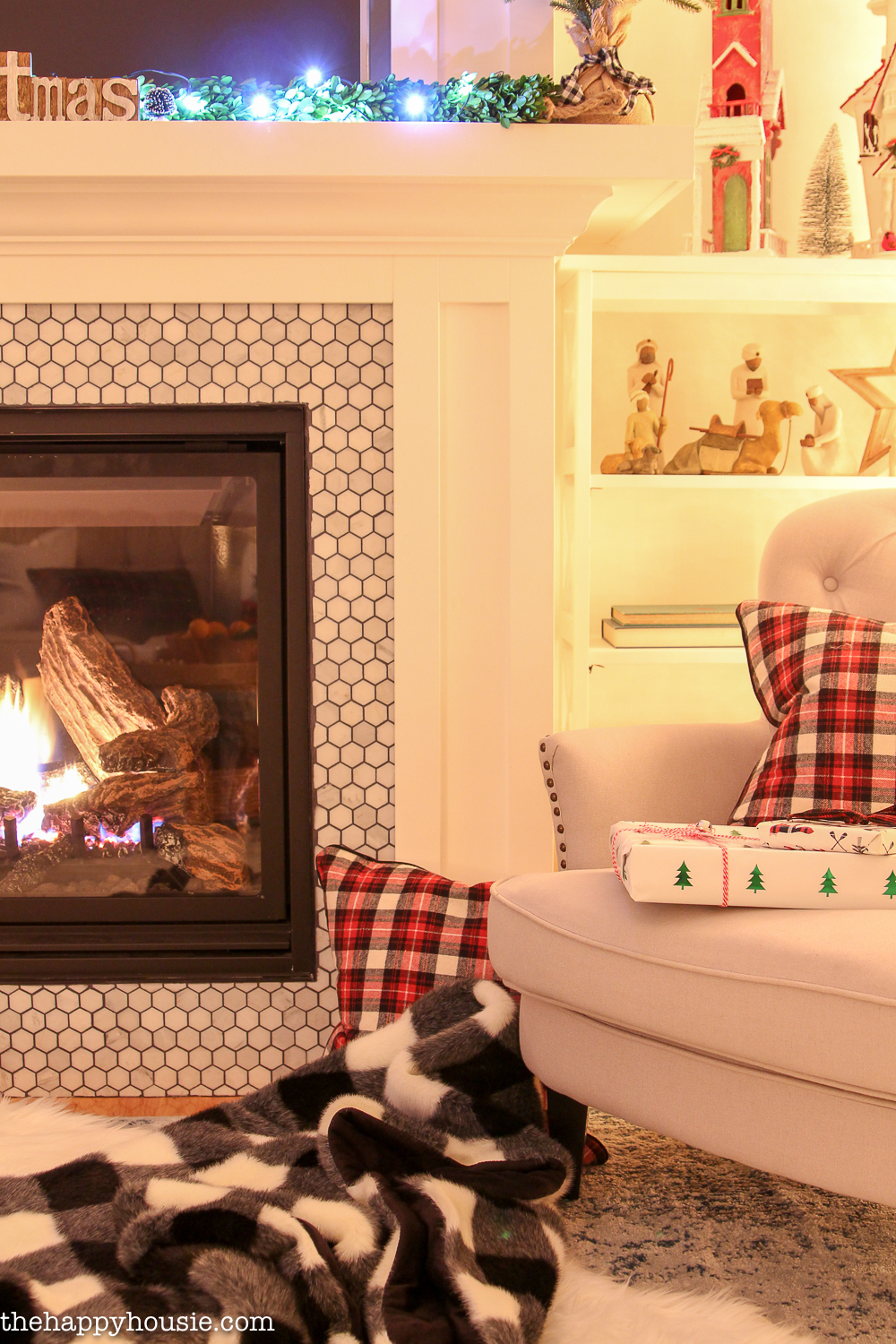 There are cozy blankets and pillows by the lit fireplace.