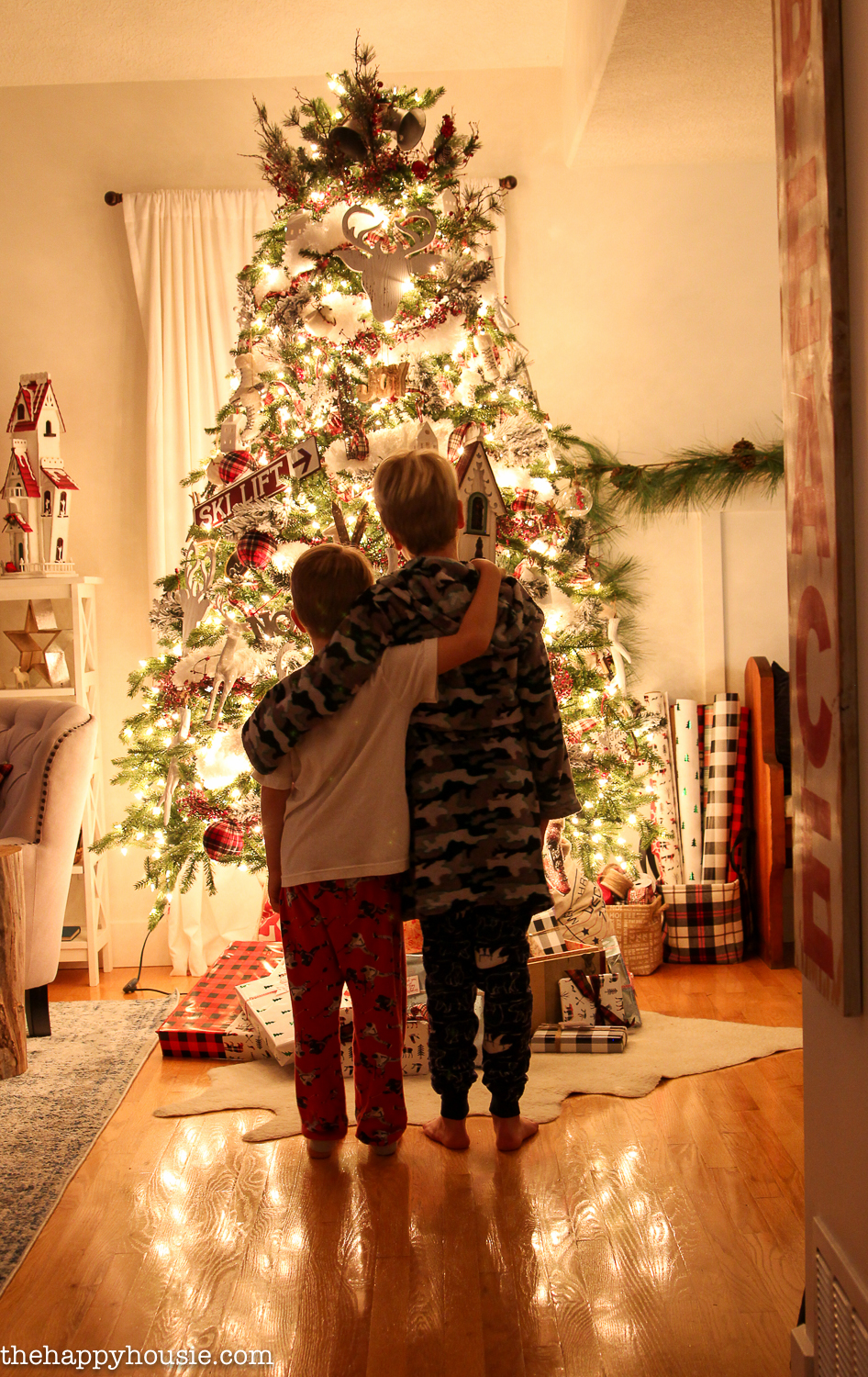 Two boys with their arms around each other standing in front of the Christmas tree.