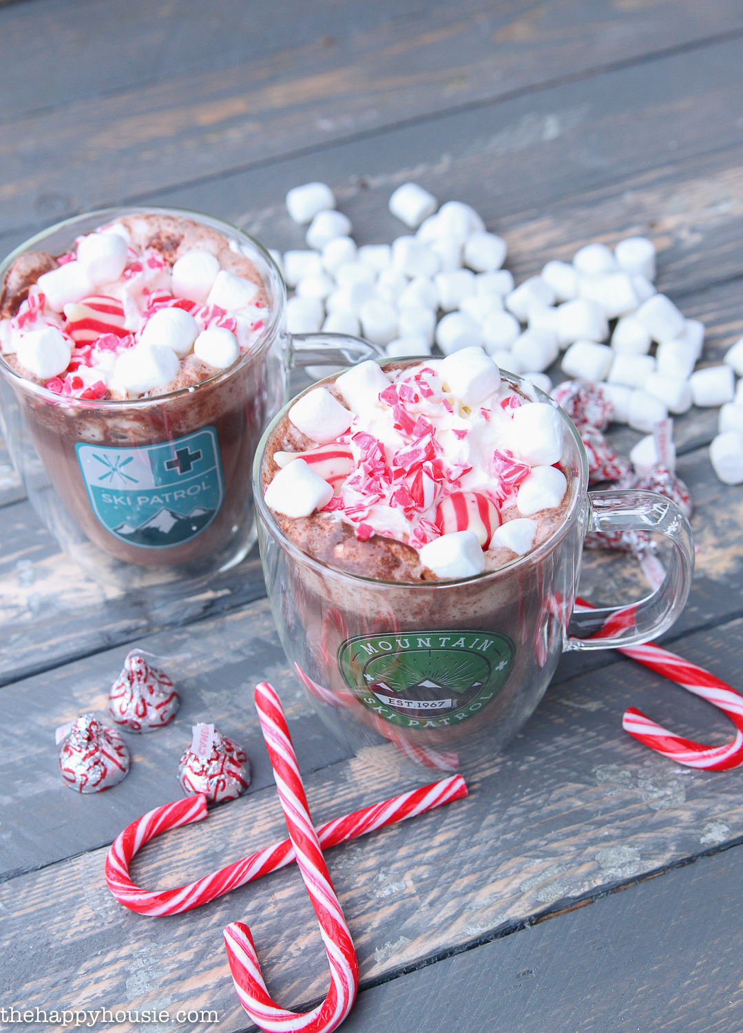 Clear mugs with hot cocoa in it and candy canes on the table beside them.