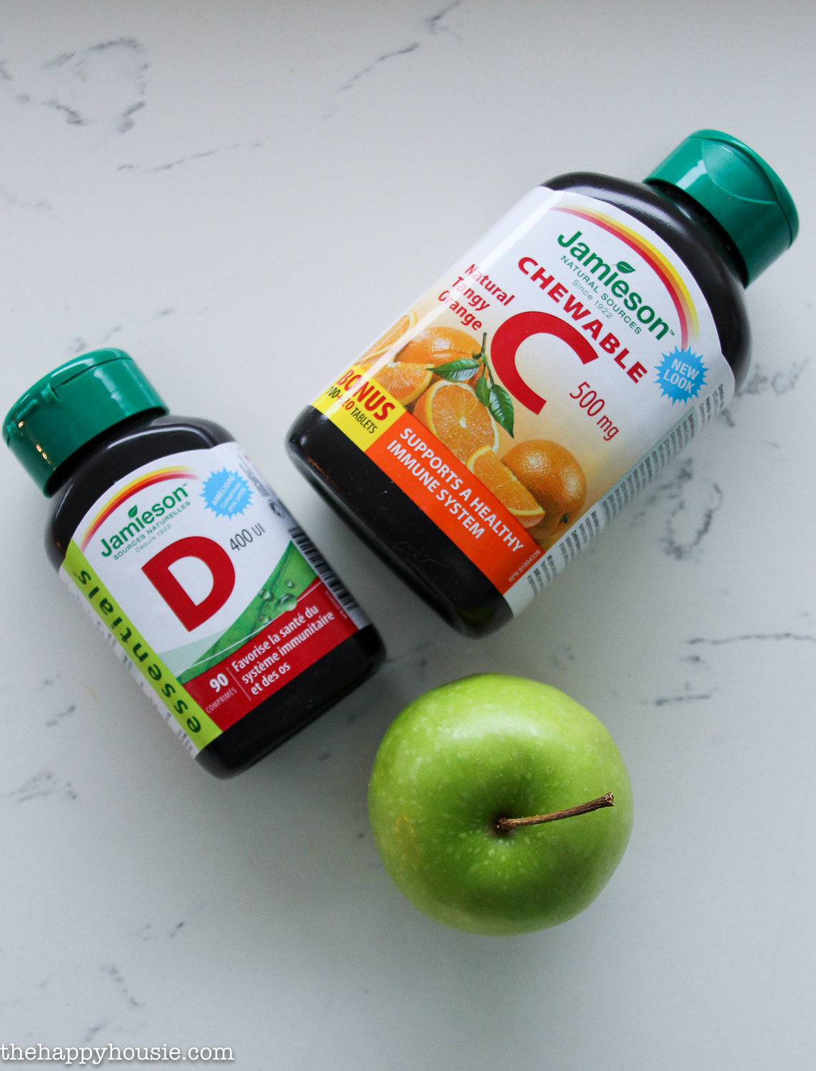 A bottle of vitamin C and D and a green apple on the counter.