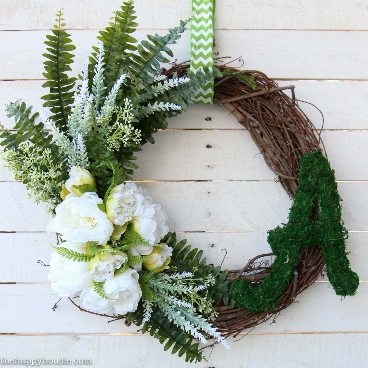 A twig wreath with lots of greenery and white flowers hanging by a white and green ribbon on the door.