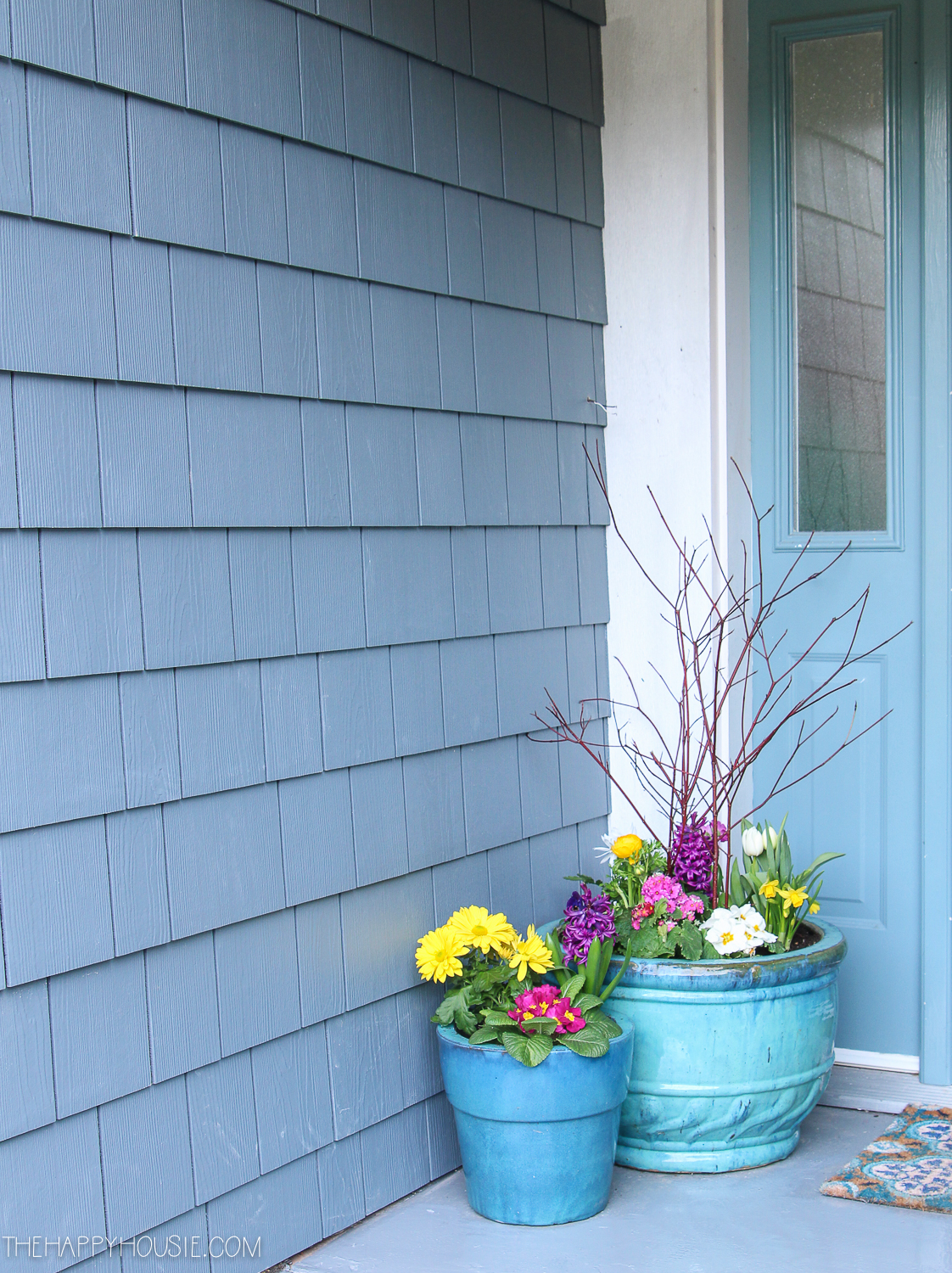 The front porch of the house with blue siding and blue flower pots.
