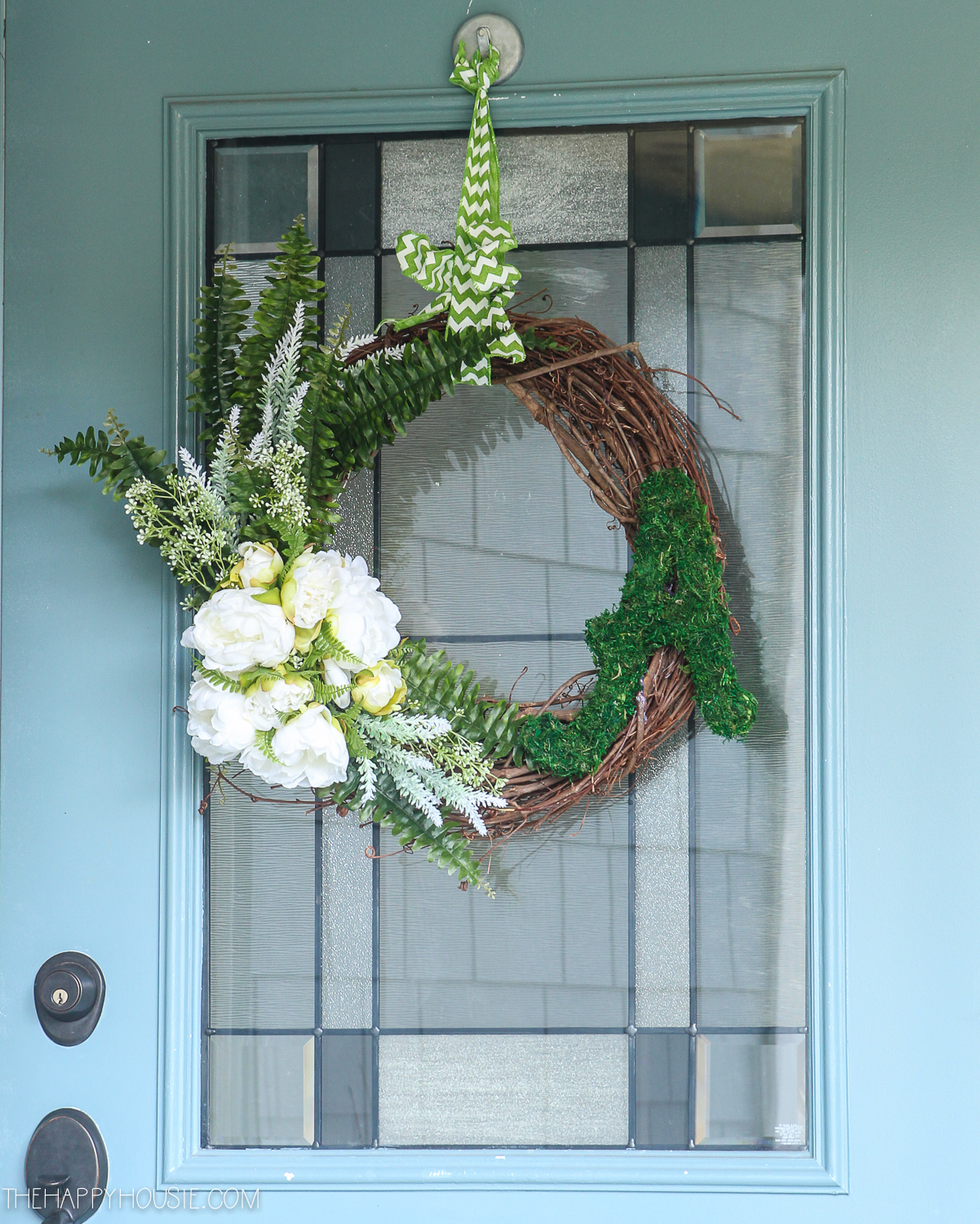 A spring wreath on the front door in tones of white and green.