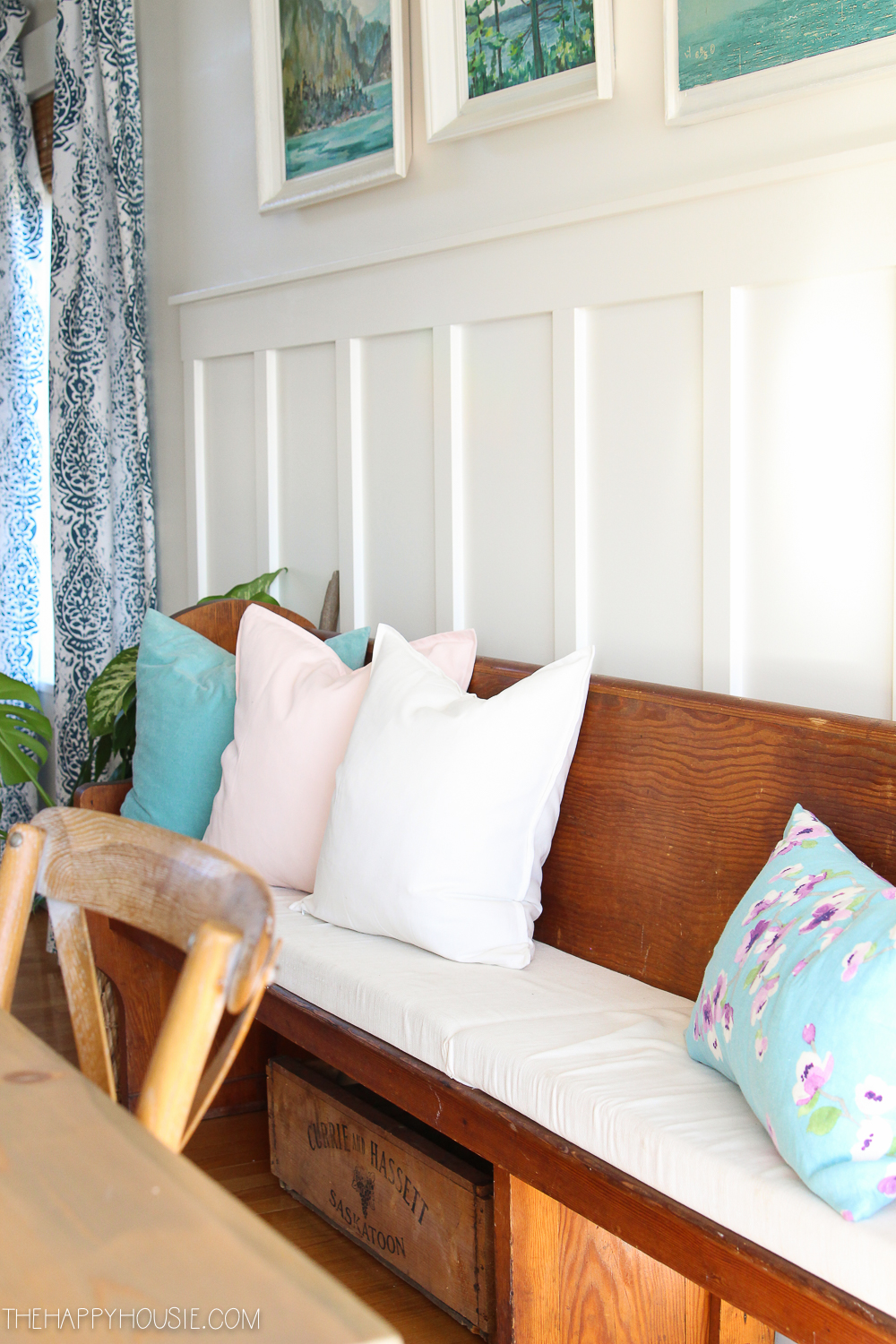 A small bench on the wall behind the dining room table with pink, white blue and floral throw pillows on it.