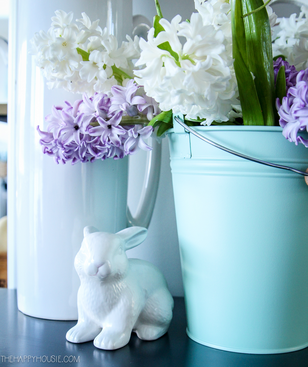 A white Easter bunny beside the blue pail with flowers.