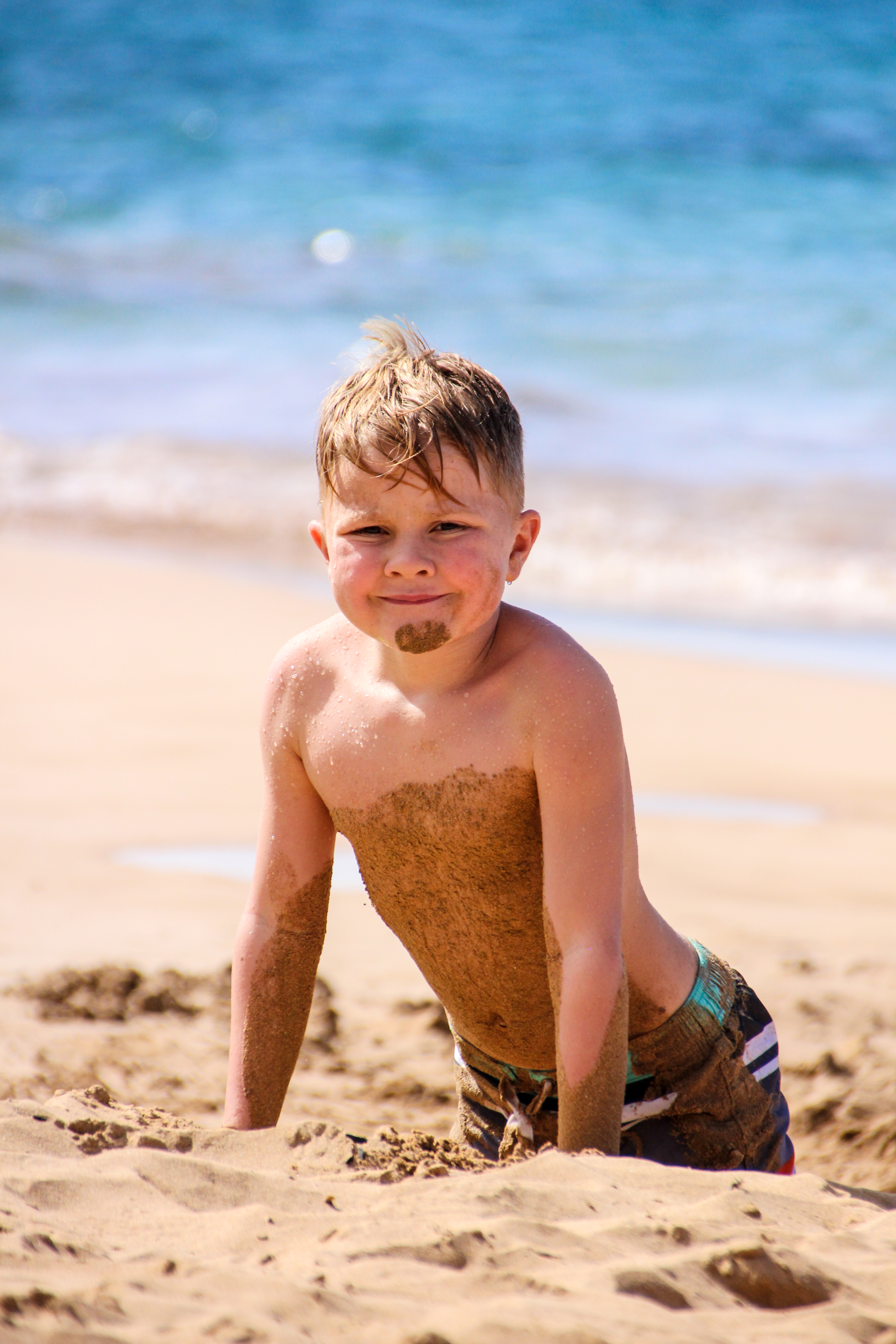A little boy is playing in the sand at the beach.