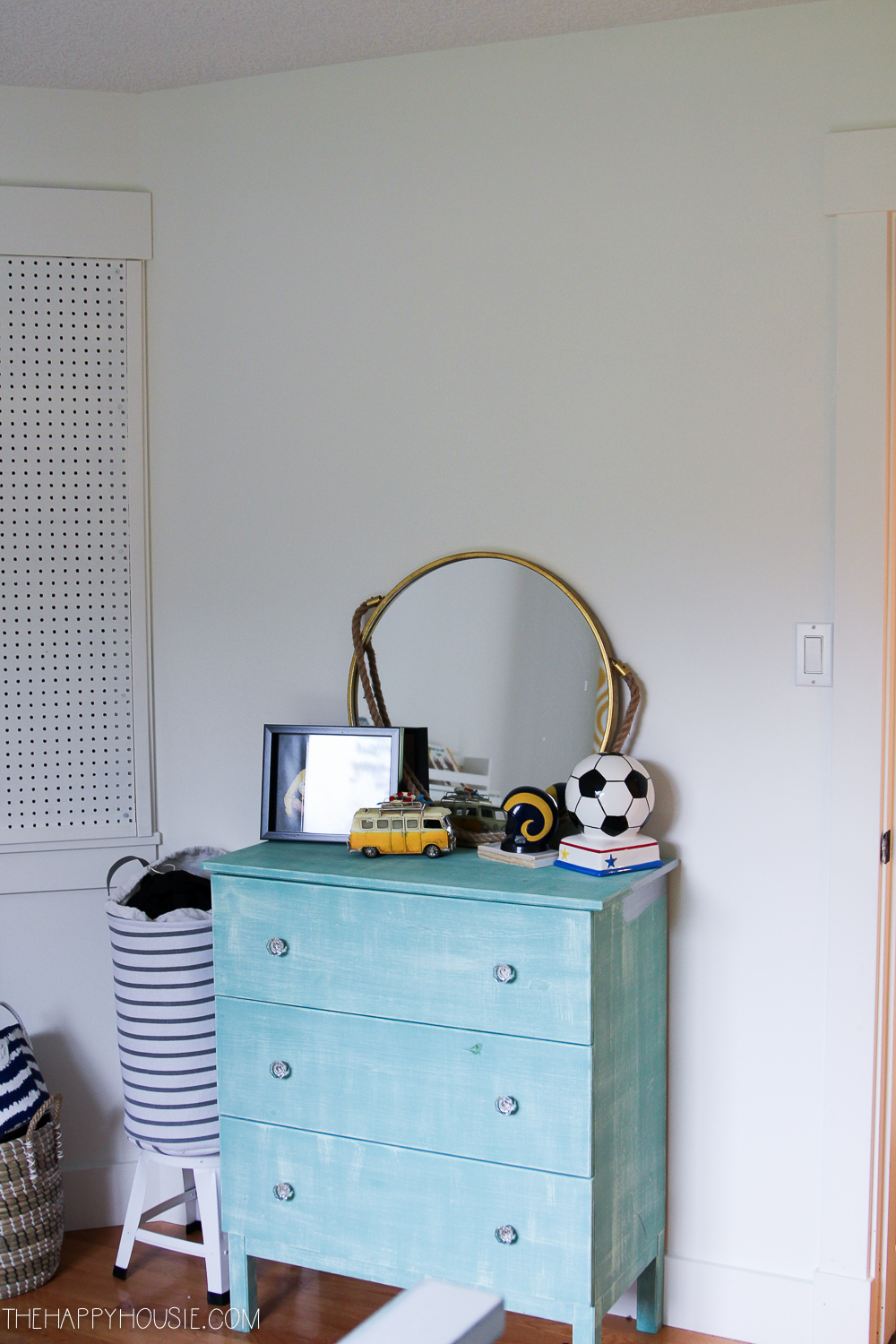 An aqua dresser has a round gold mirror on it and a small soccer trophy.