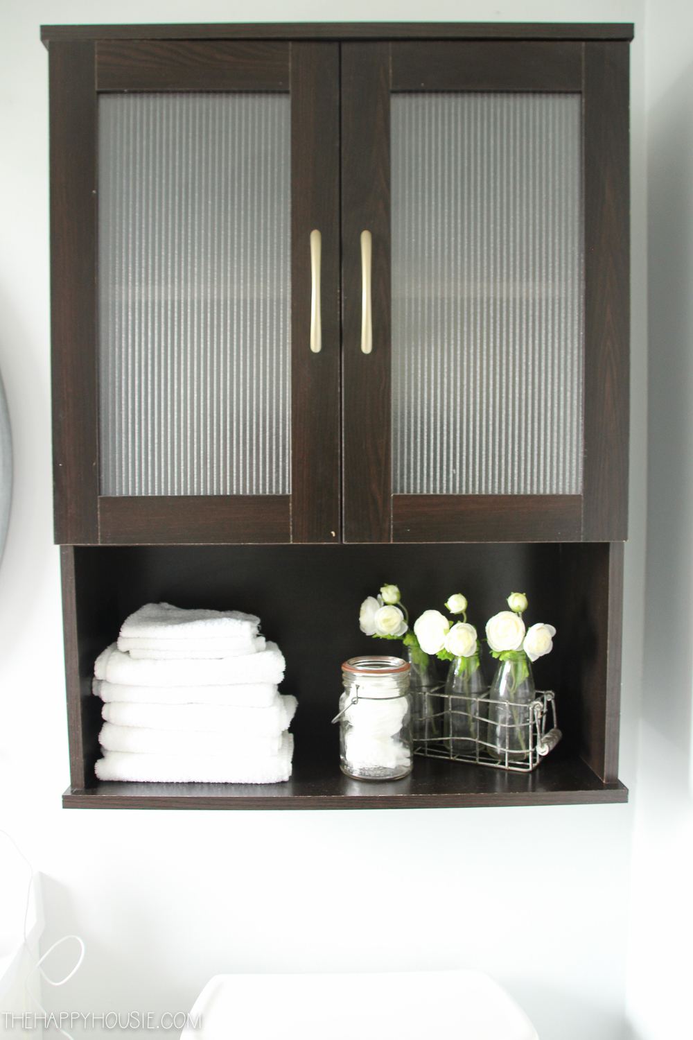 A brown cabinet with white towels and white flowers.