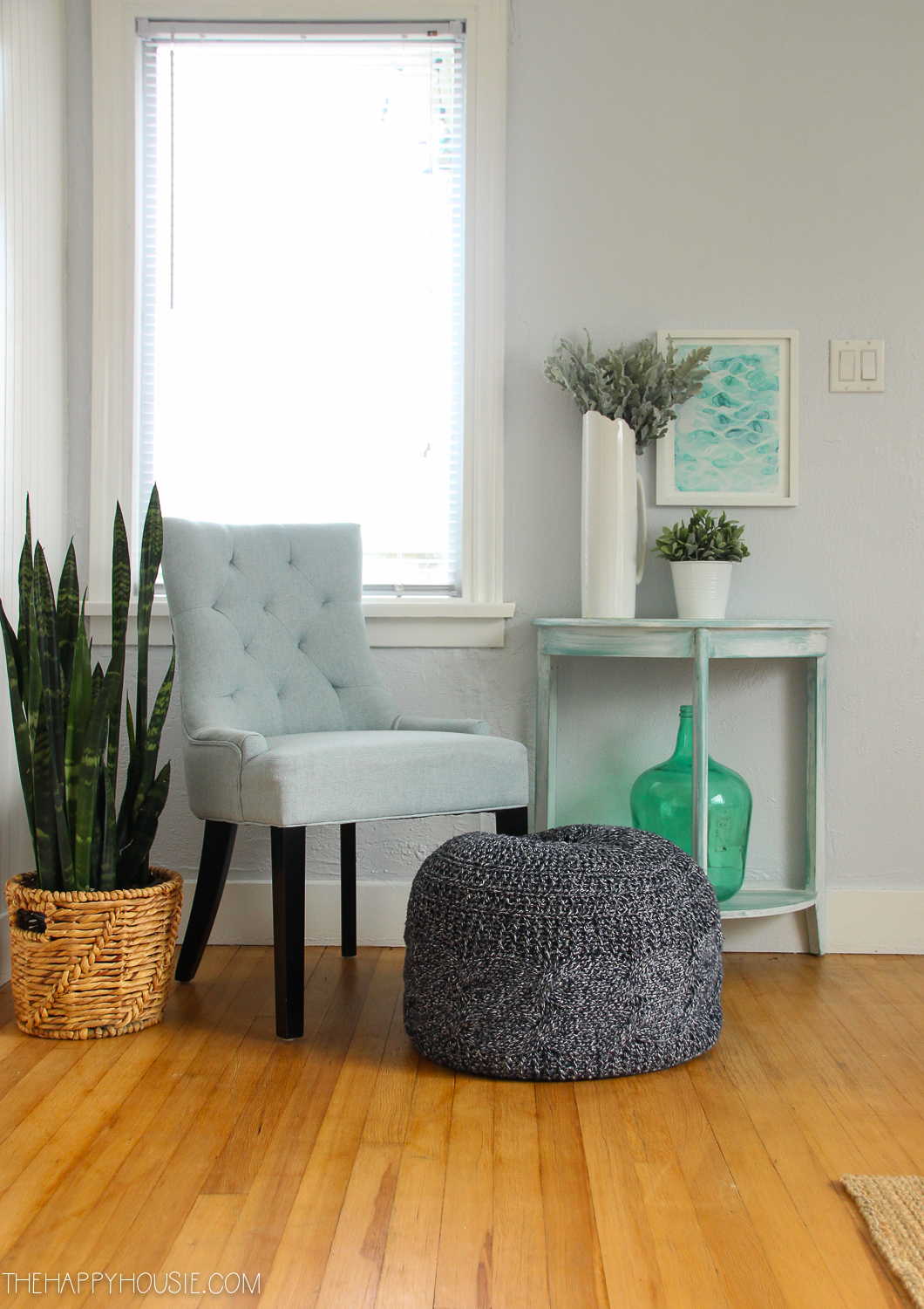 There is a pouf in front of a tufted blue chair.