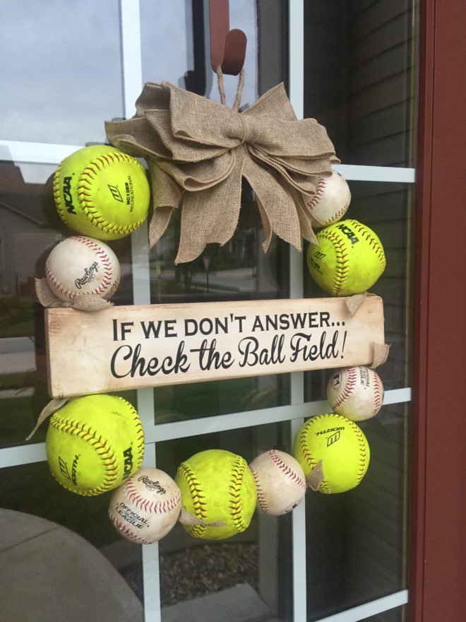 A wreath made up of baseballs with a neutral bow hanging on a door.