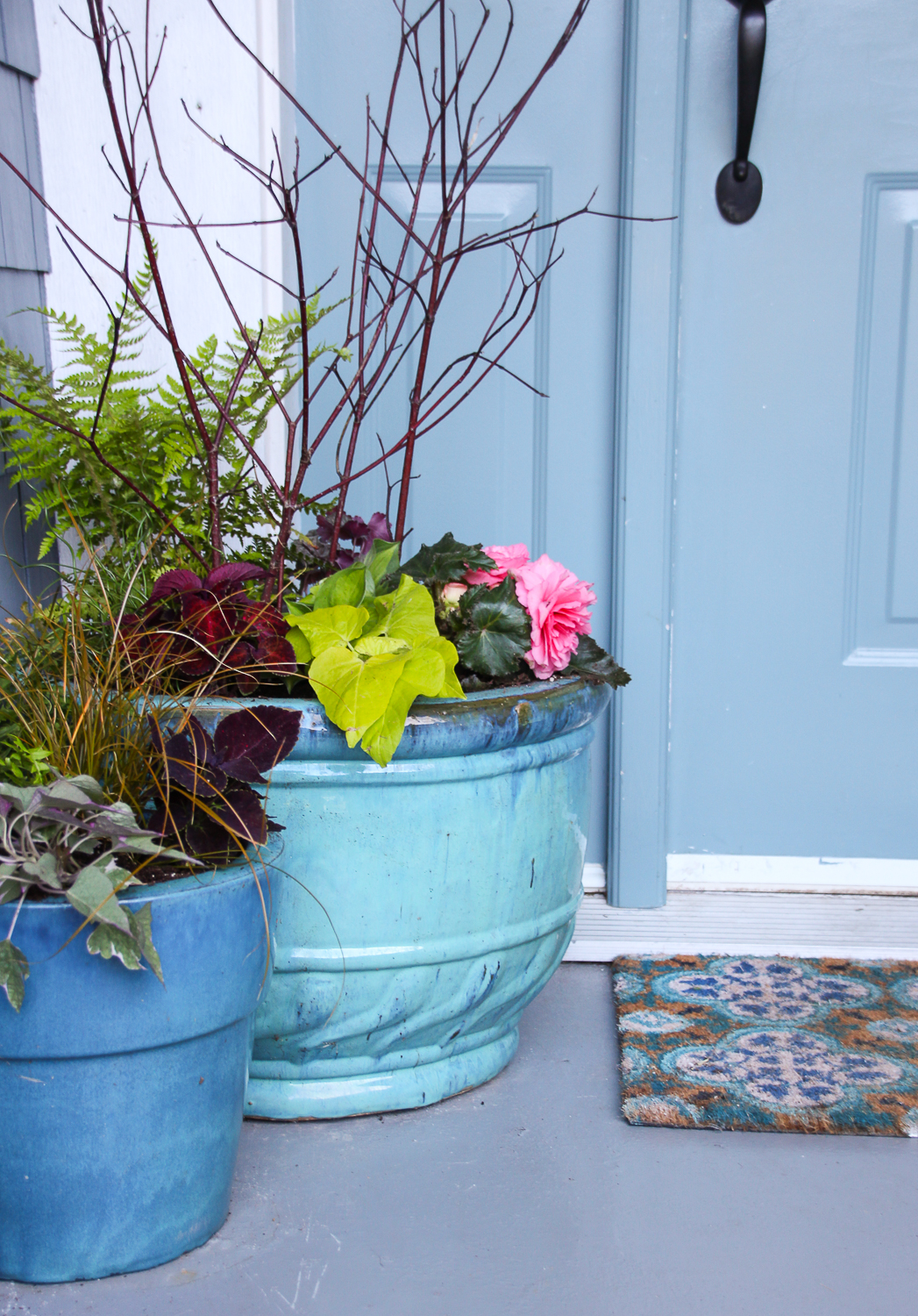 The front door of a house with a porch mat and the shade garden pots beside it.