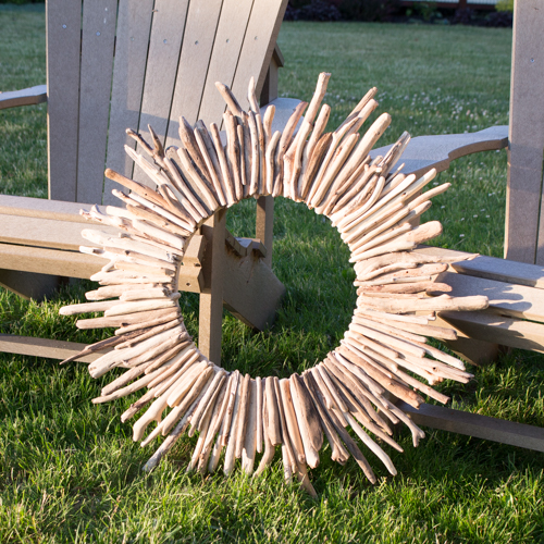 A large driftwood wreath beside two wooden chairs on the grass.