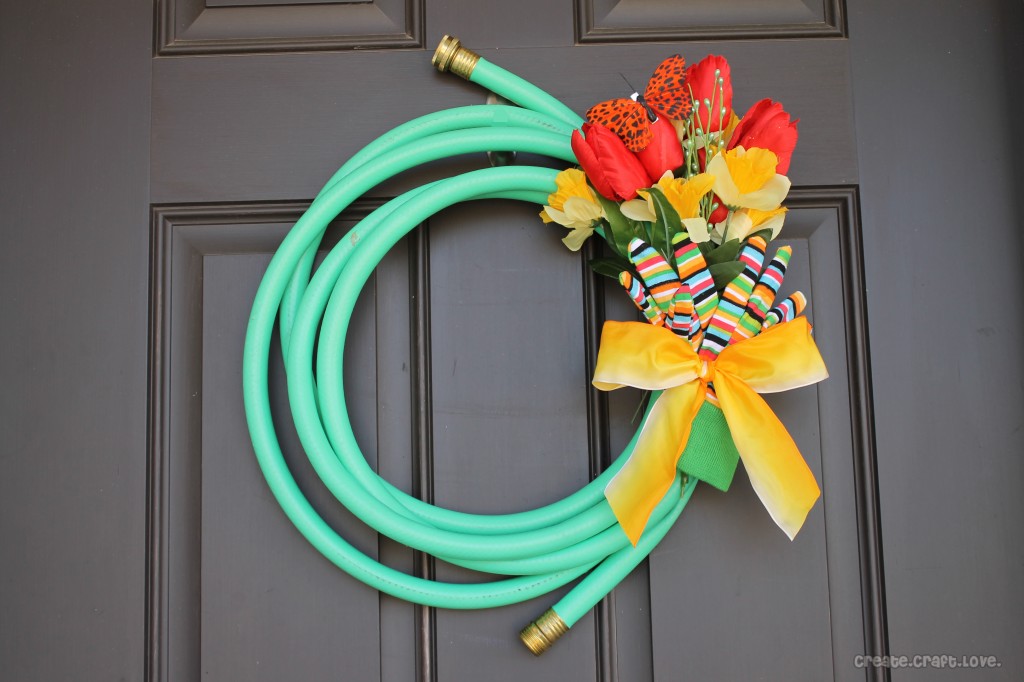A garden hose with red and yellow flowers forming a wreath hanging one a dark brown door.
