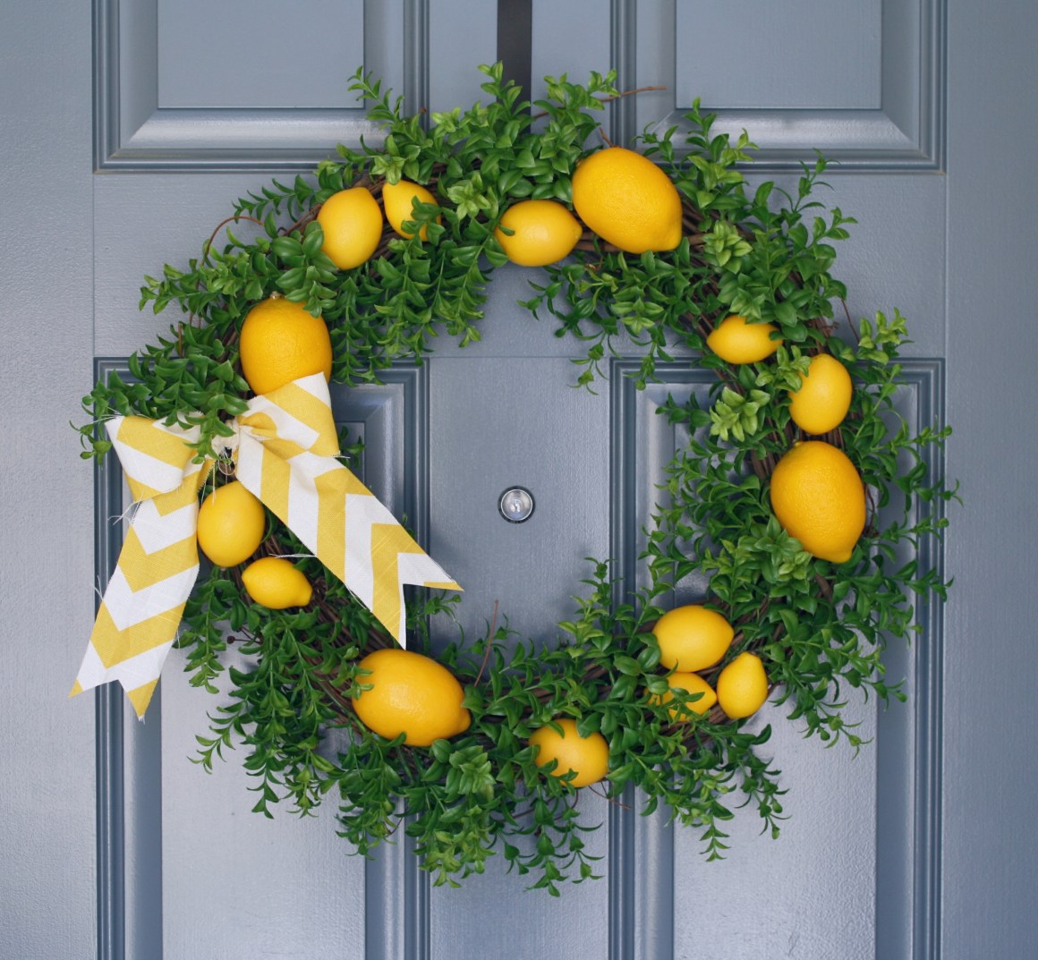 A green wreath with yellow lemons on it and a white and yellow bow, hanging on a slate blue door.