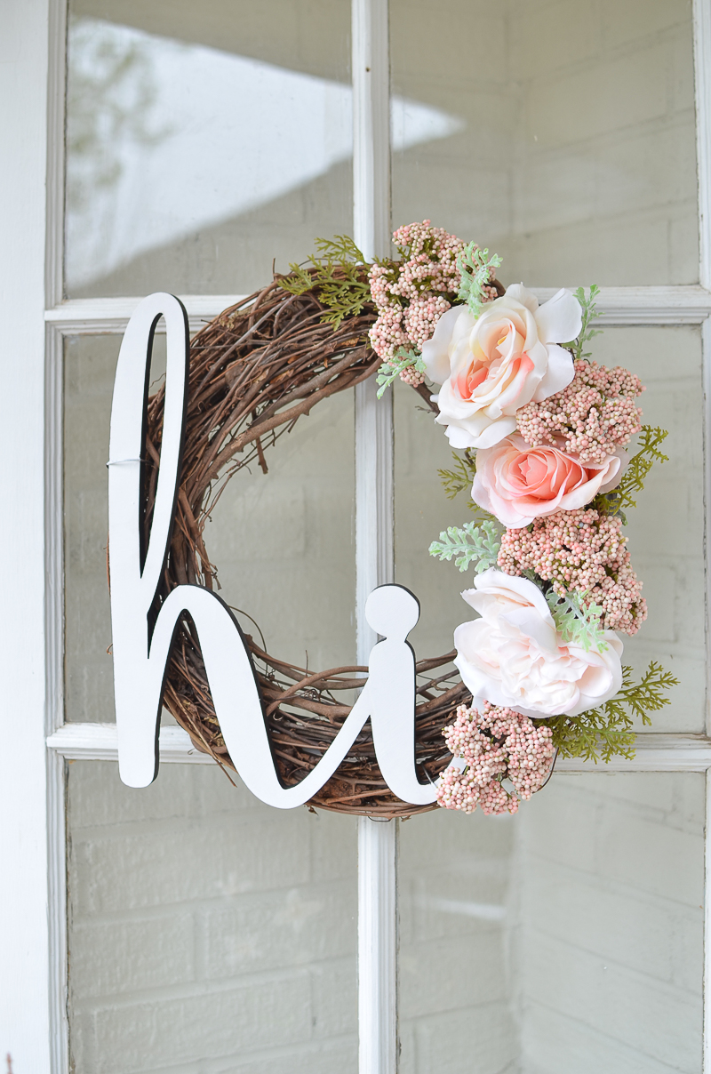 A twig formed wreath with white and blush pink flowers and a white sign saying hi.