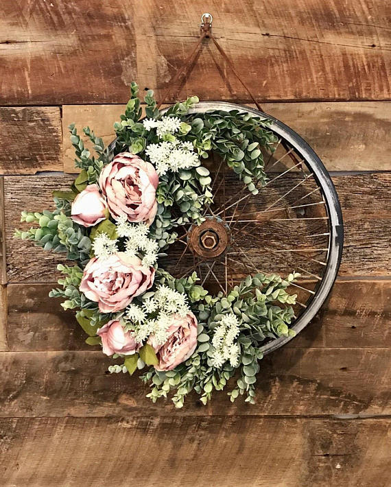A bicycle wheel with pink flowers and greenery on it hanging on a wooden wall.