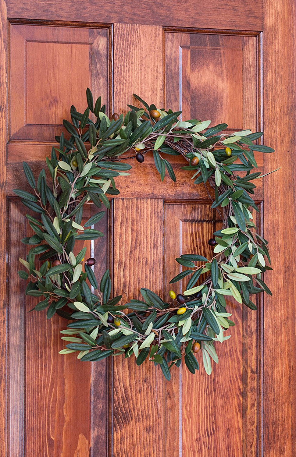 A large olive green leaf wreath with small olives on it hanging on a dark wooden door.