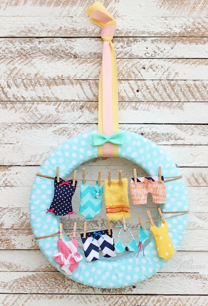 A blue and white polka dotted wreath with miniature swimsuits hanging on small clothesline.