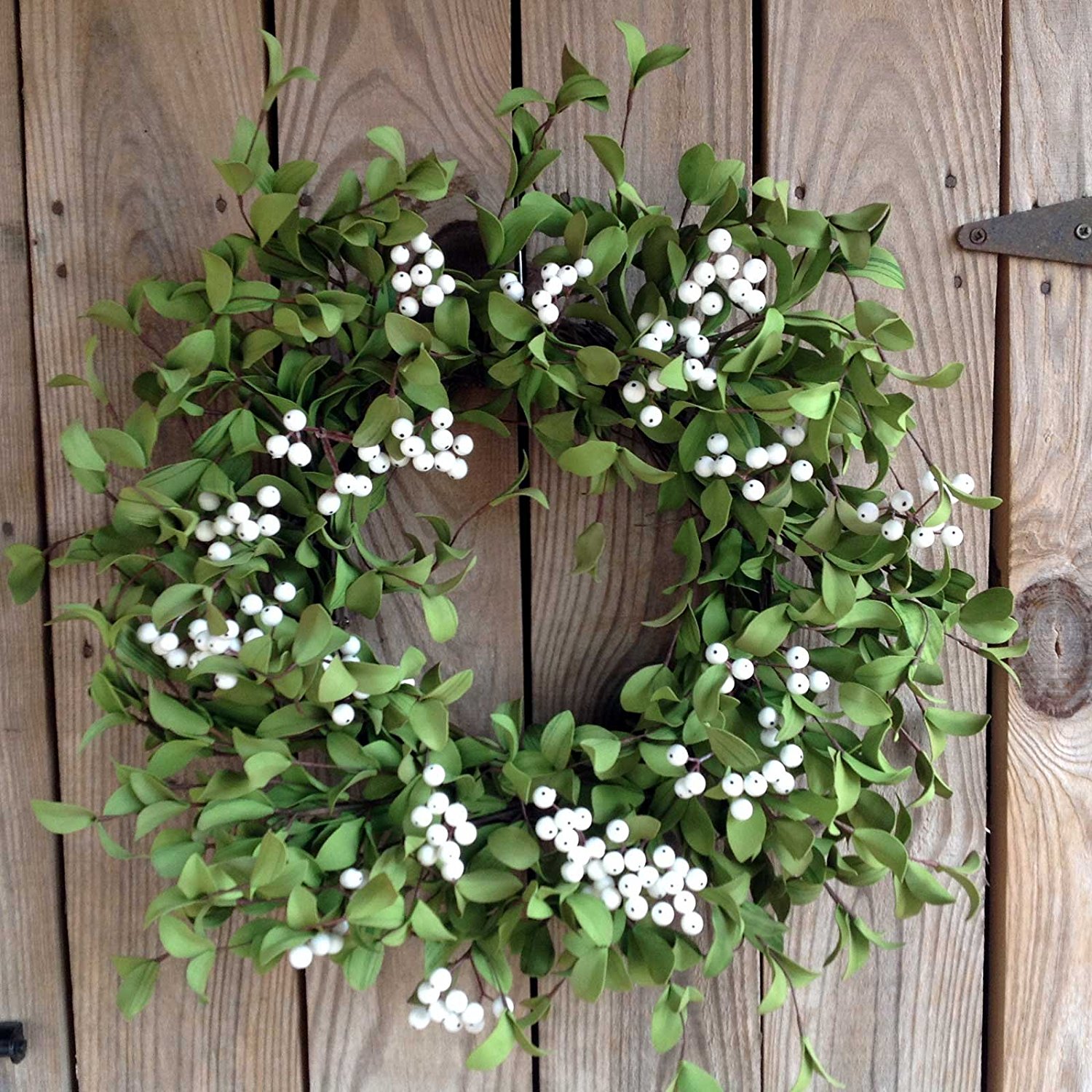 A large greenery wreath with white berries on a wooden door.