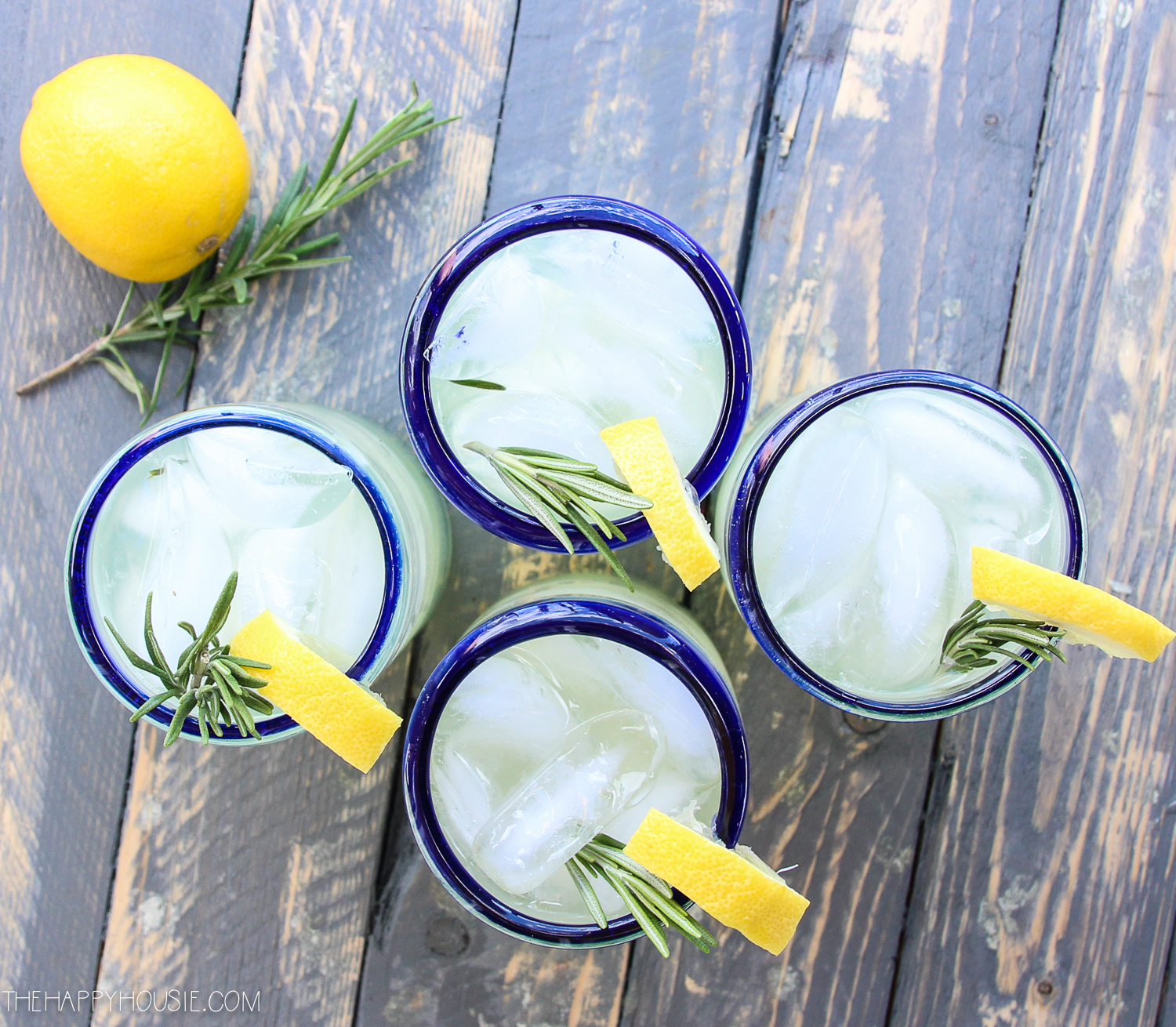 Clear glasses with blue rims and a sprig of rosemary with a slice of lemon on the rim.