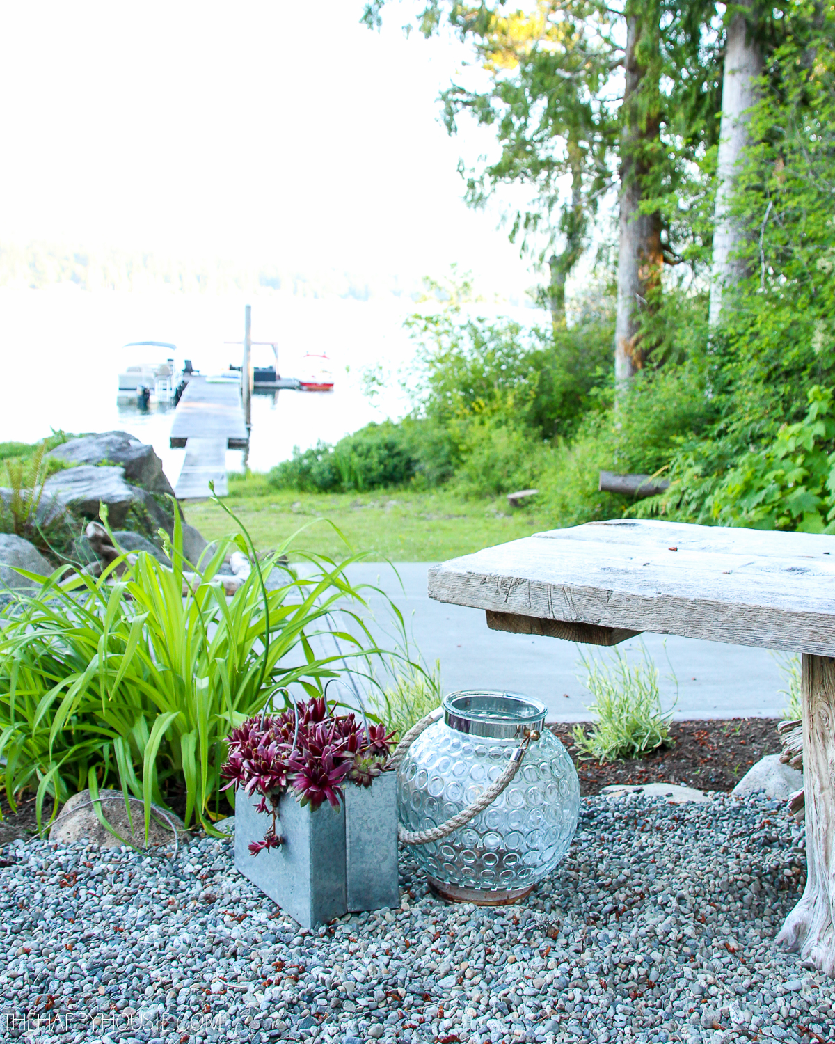 A small garden with a wooden bench, an outdoor candle and a container with succulents.