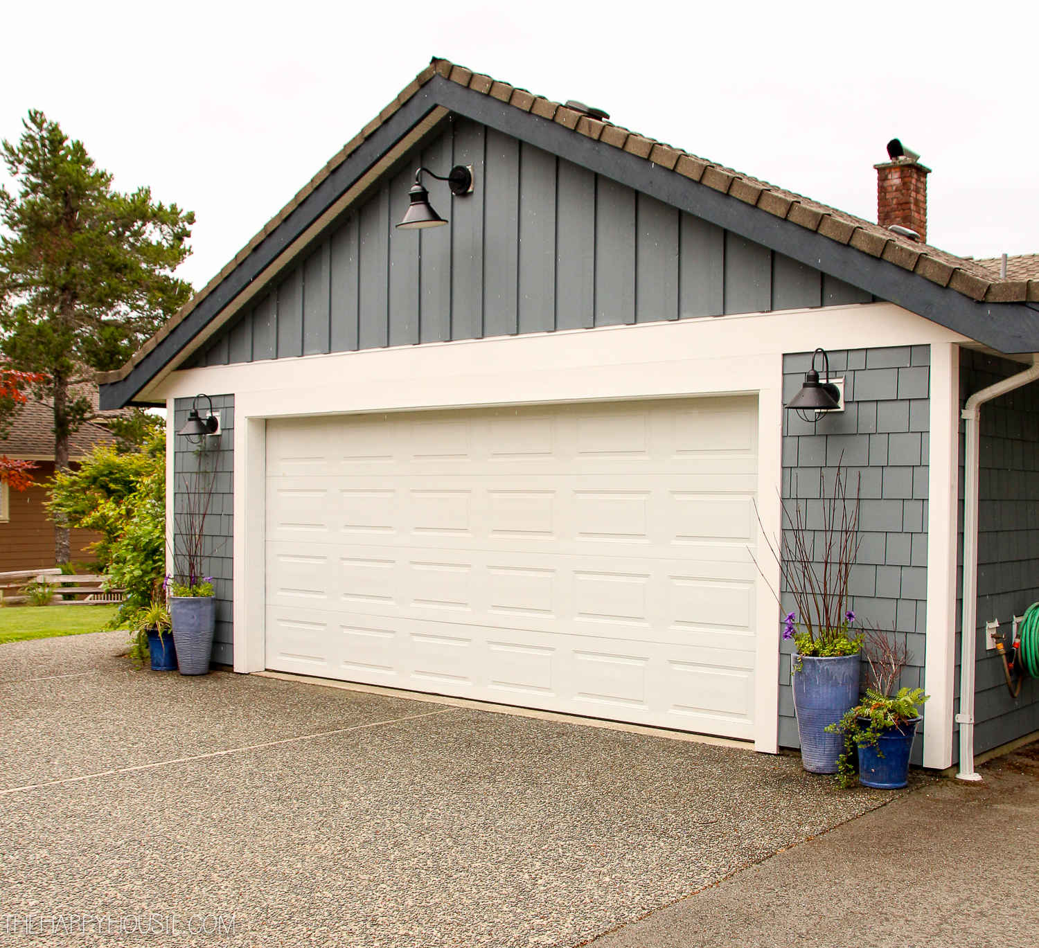 A white garage door flanked by pots of greenery with outdoor lights.