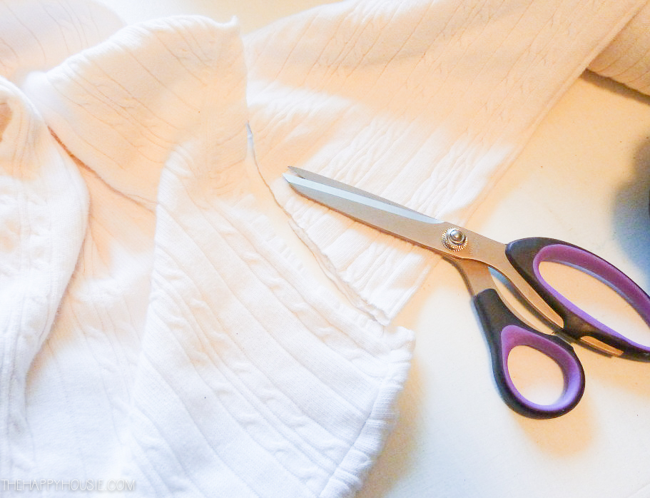 A white sweater being cut for the pumpkin with a pair of scissors beside it.