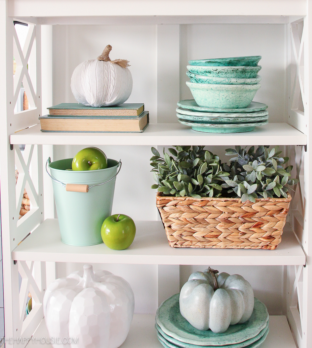 Open shelves with a bucket of green apples, green dishes and white pumpkins.