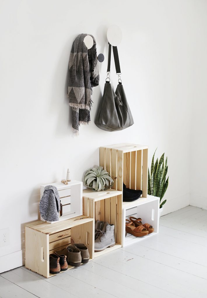 Crates on the ground with boots and shoes and bags and scarves hanging on the wall.