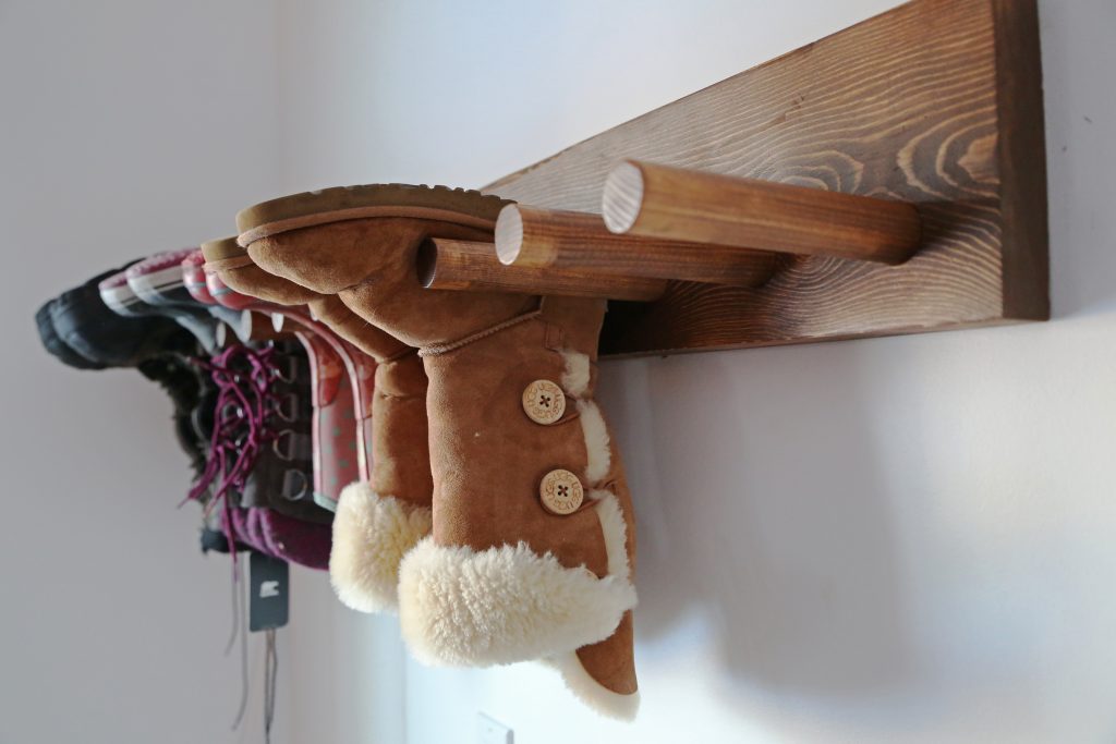 A wooden peg with boots hanging from it upside down.