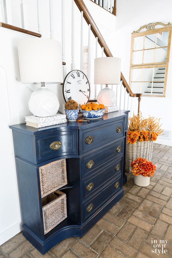 A blue grey chest of drawers in the entryway with pops of amber flowers.