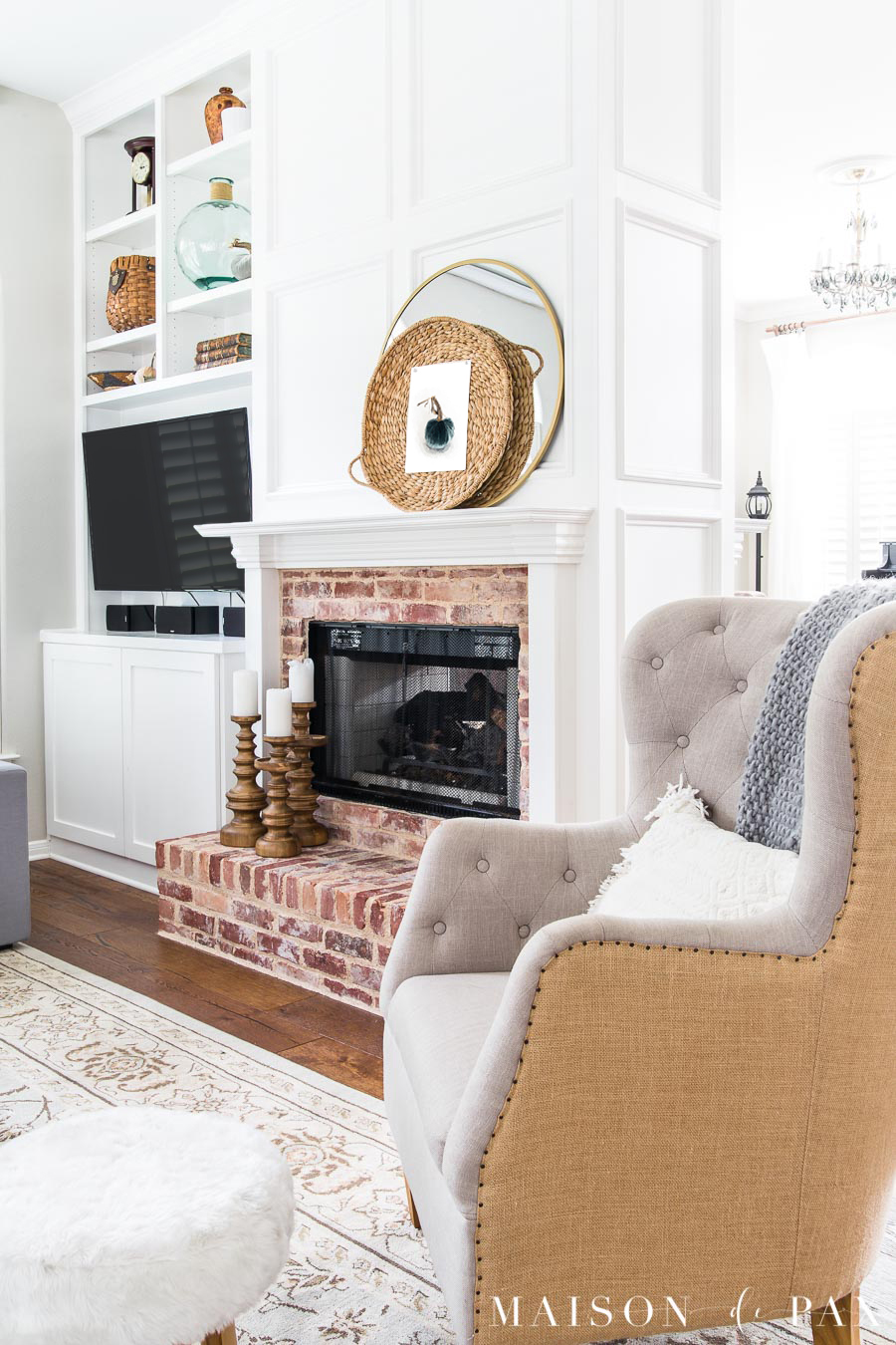A neutral armchair in the corner of a room beside a fireplace.