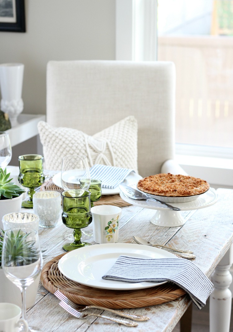 A table setting with green glass and a pie is on the table.