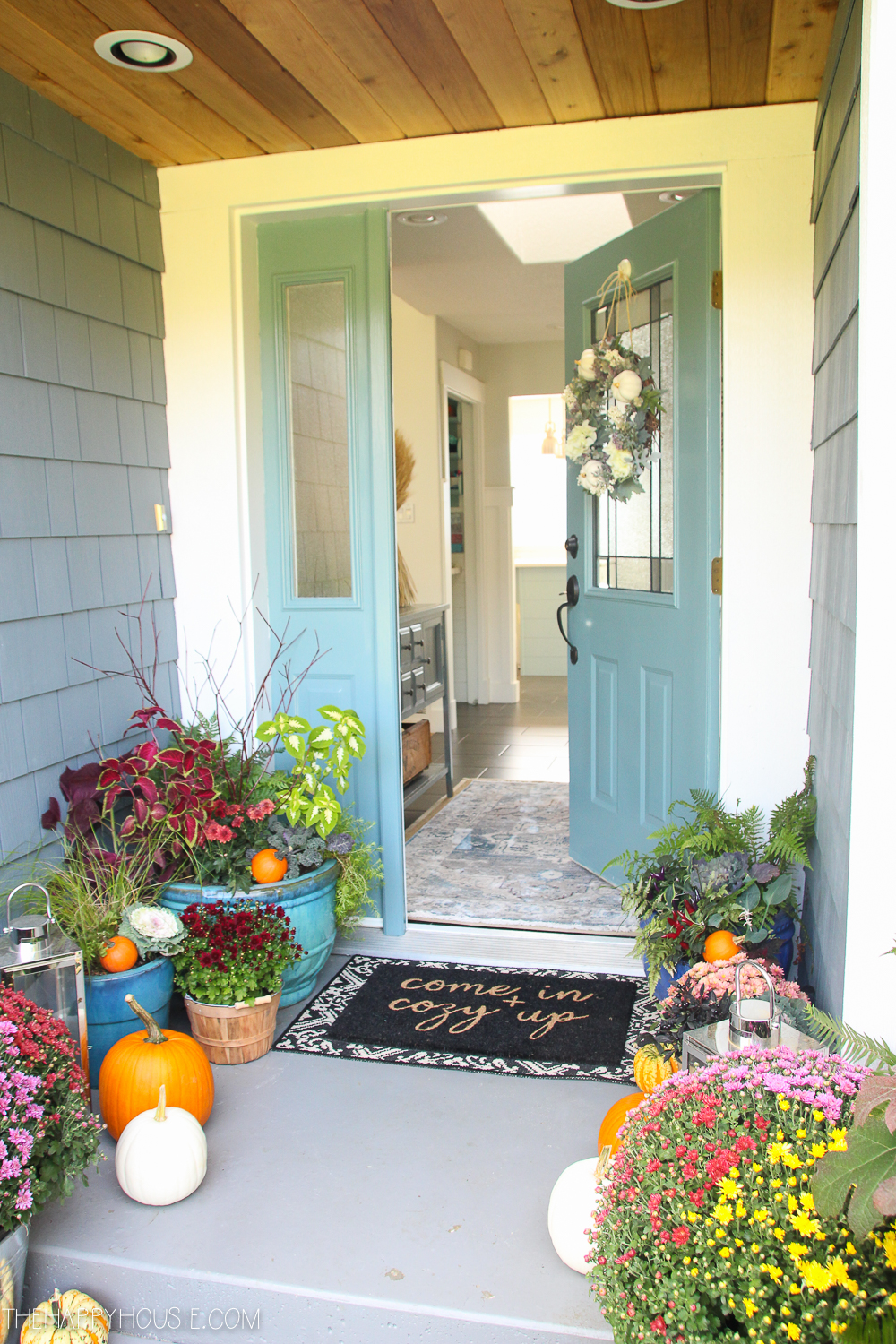 The front door ajar with planters of flowers and green plants.